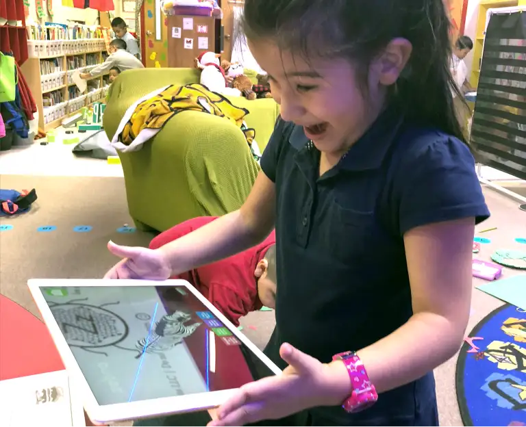 Child having fun and smiling while using the Letters Alive app on a tablet