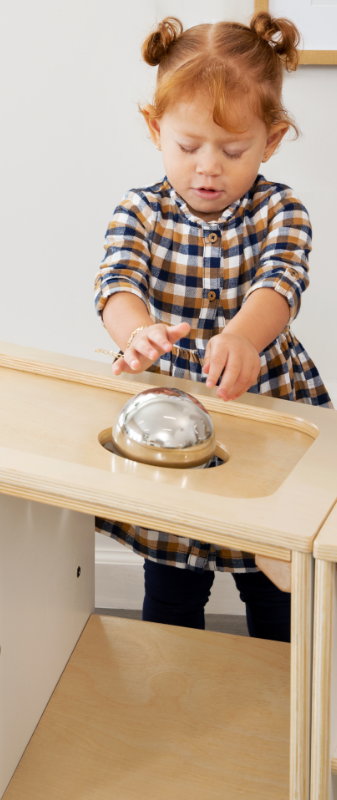 Girl rolling ball down top of Angled Stoarge unit and into a hole