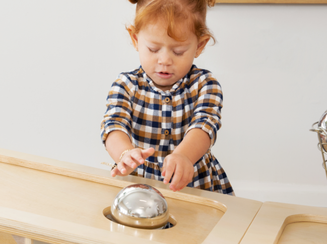 Girl rolling ball down top of Angled Stoarge unit and into a hole