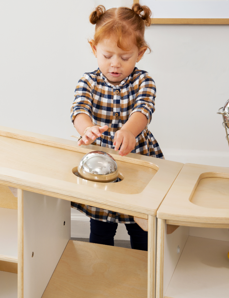 Girl rolling ball down top of Angled Stoarge unit and into a hole