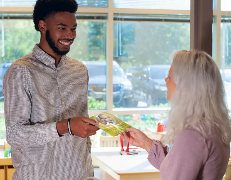 Teacher handing a parent a copy of Promoting Resilience For Now and Forever booklet