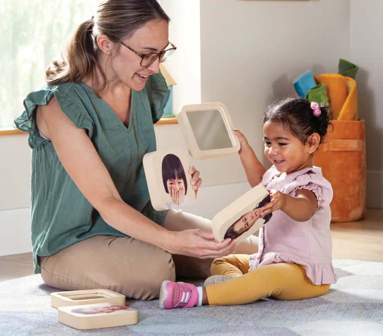 Teacher and toddler on a classroom carpet using foam images of different emotions