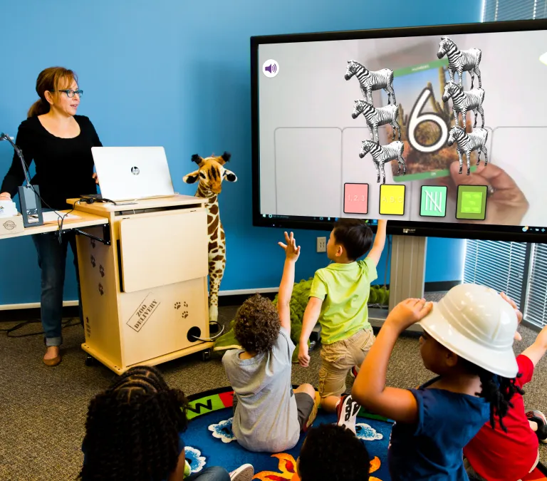 Teacher operating a large display showing Alive Studios to a preschool class