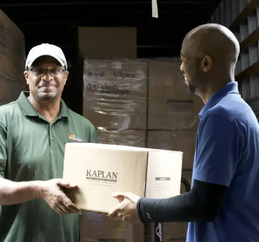 Two delivery drivers unloading a brown Kaplan box from the back of a box truck