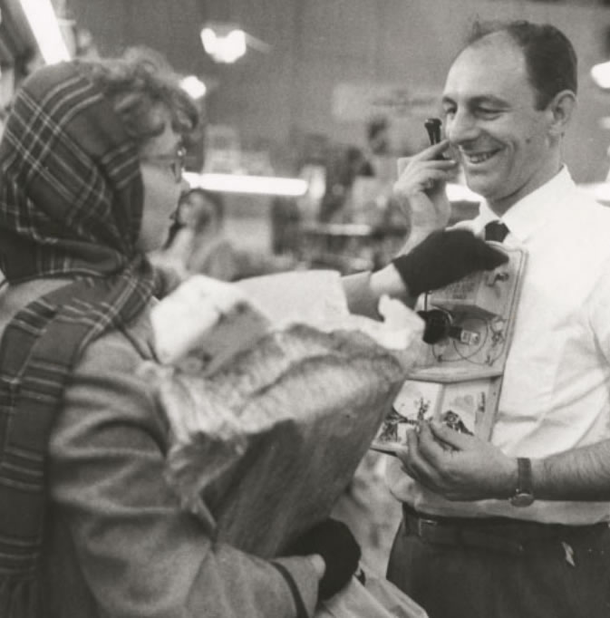 Black and white photo of Leon Kaplan helping a customer