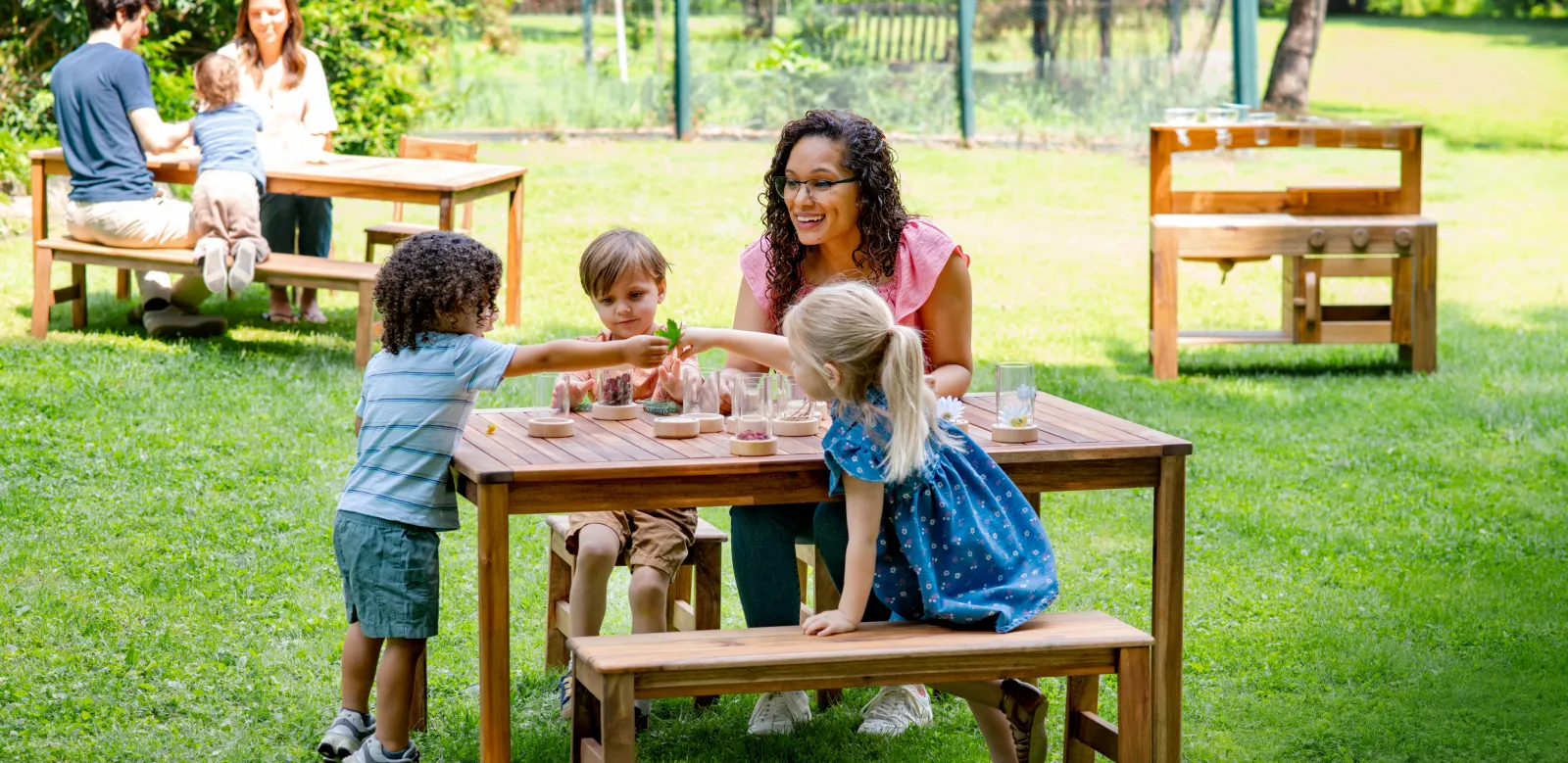 Teacher and children around a wooden table outside paying with manipulatives