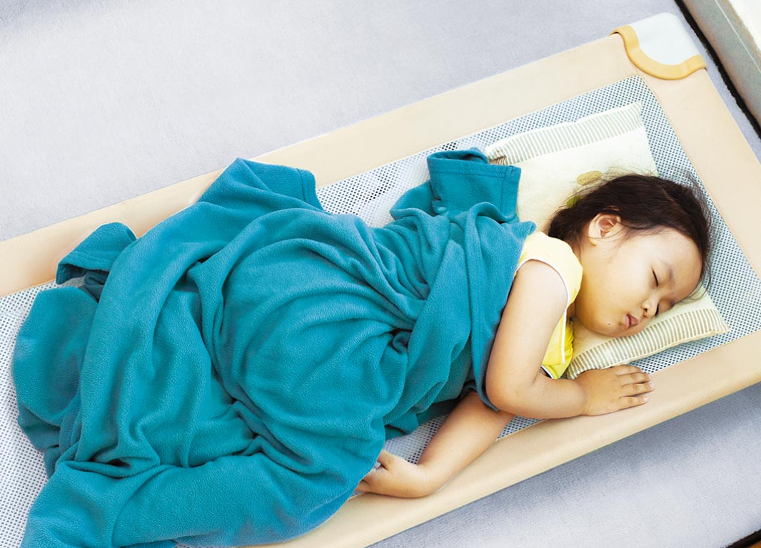 Child taking a nap on a cott with a blue blanket