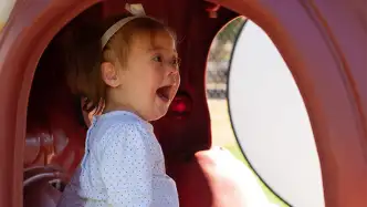 Toddler child sitting inside an outdoor playset tunnel laughing