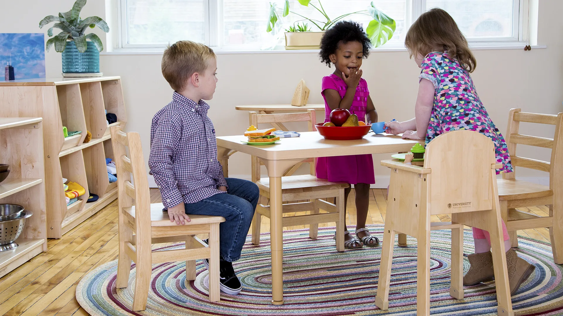 Three young children playing around a table in a preschool classroom