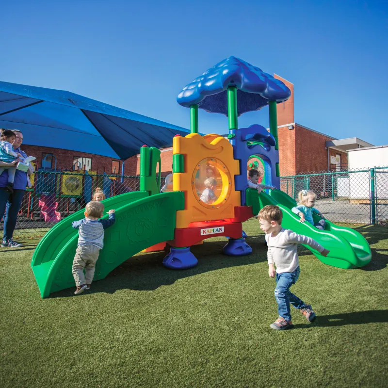 Children playing on a playground set next to a preschool building