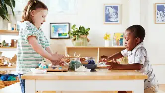 Two young children at a classroom table playing with toy food