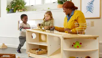 Children and teacher playing around a small shelving unit in a classroom