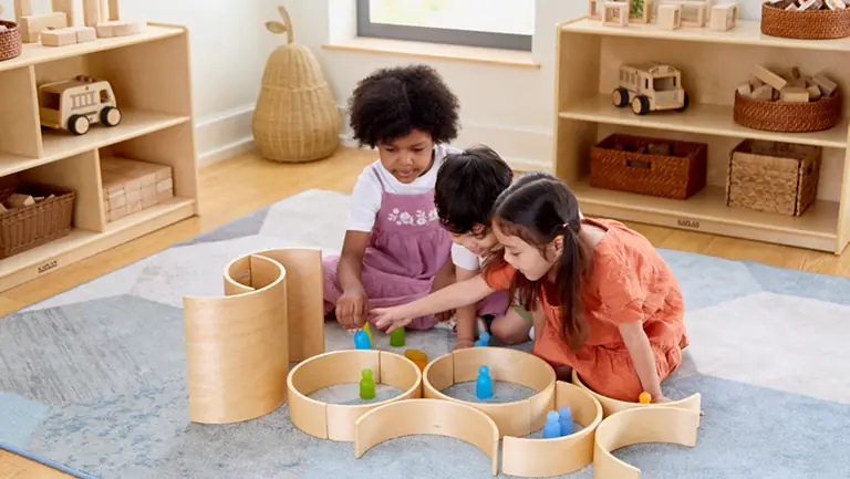 Three young children playing with wooden arch toys in a preschool classroom