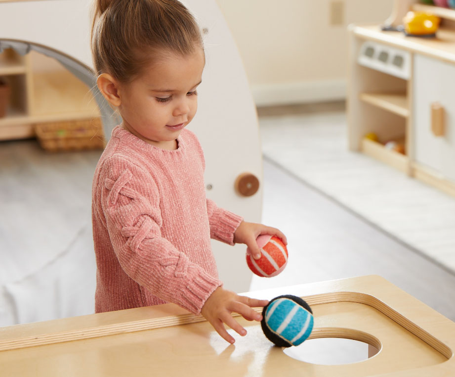 Child rolling balls into a hole in the top of the Activity Island unit