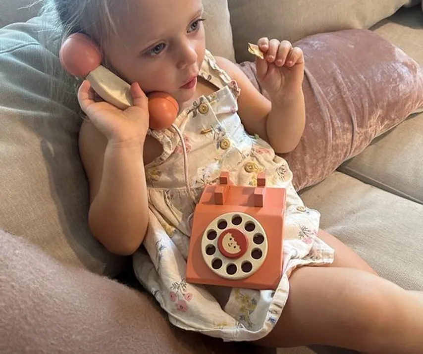 Young child playing with a wooden toy rotary phone