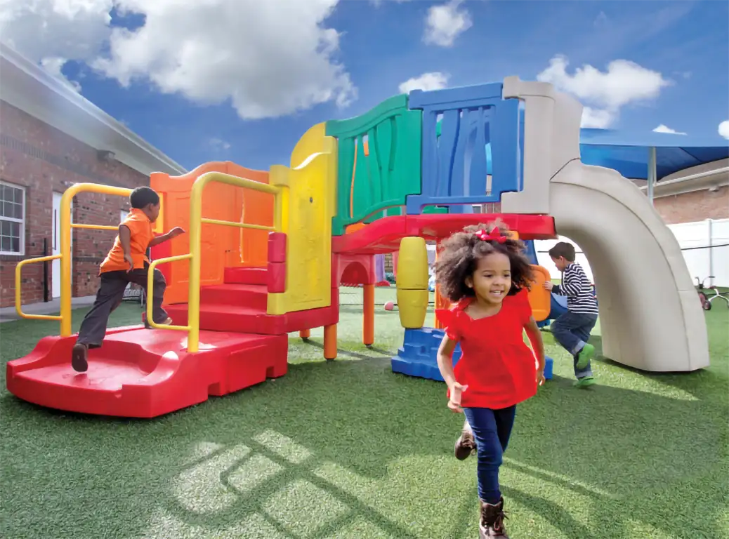 Young child running in front of a colorful playground set with other children playing in the background