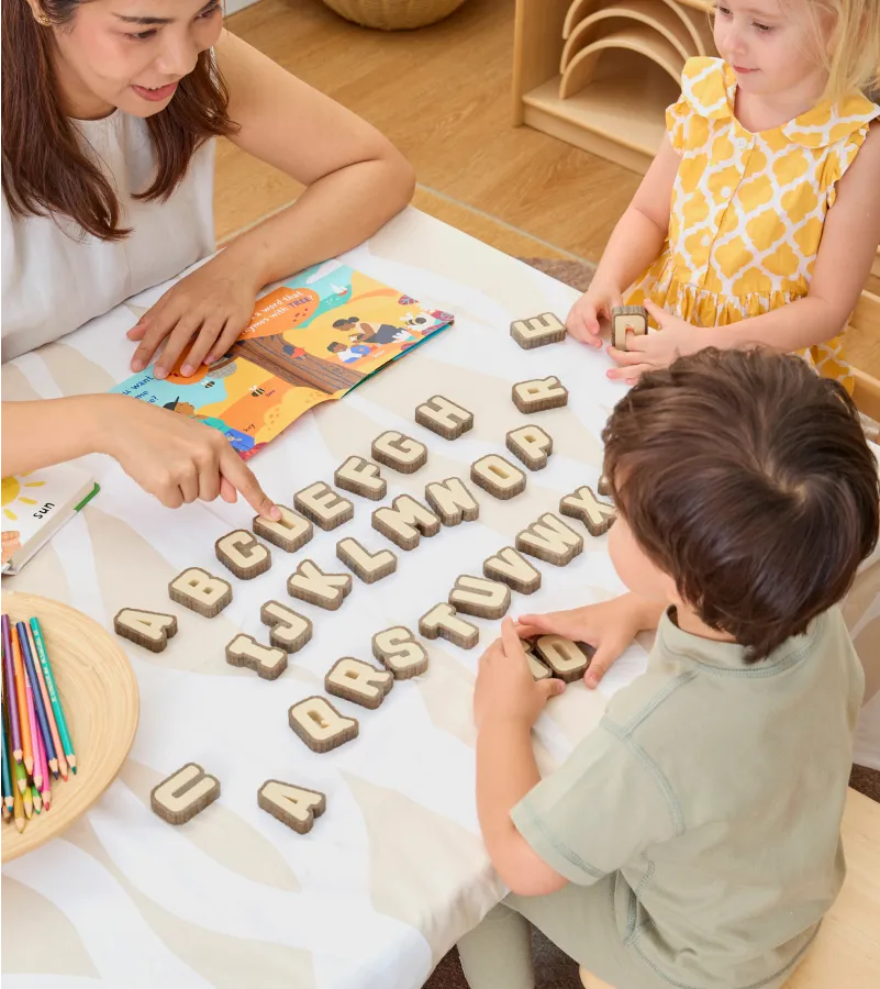 Teacher and children placing colorful letter-shaped magnets on a board