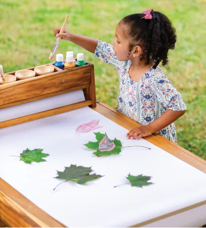 Girl outside painting leaves on a large roll of paper stretched across a table