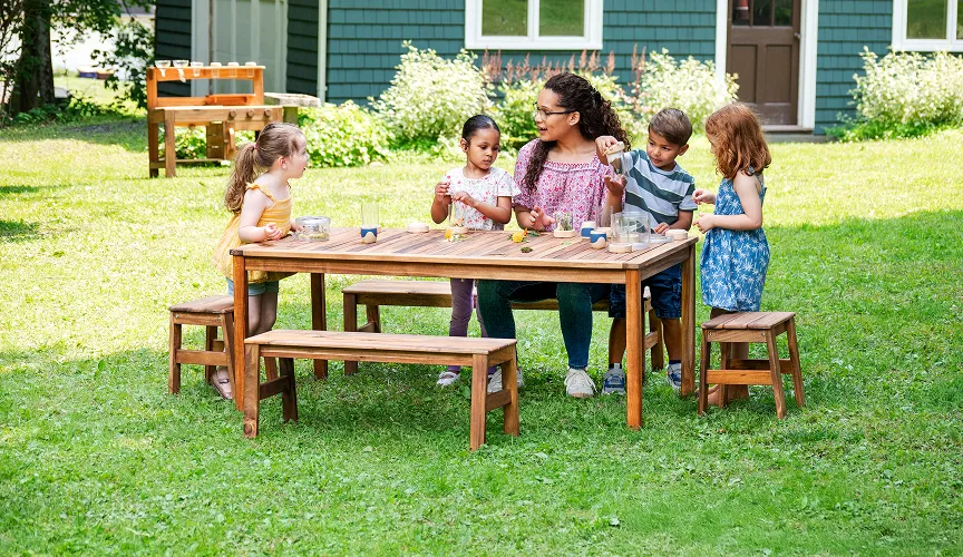 A teacher and children playing outside around the Acadia wooden table