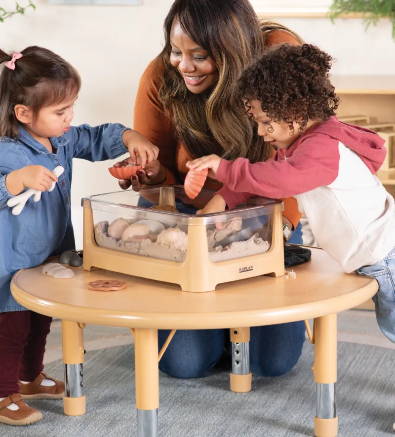 Teacher and two small children playing in a tabletop sand box with different shaped seashells