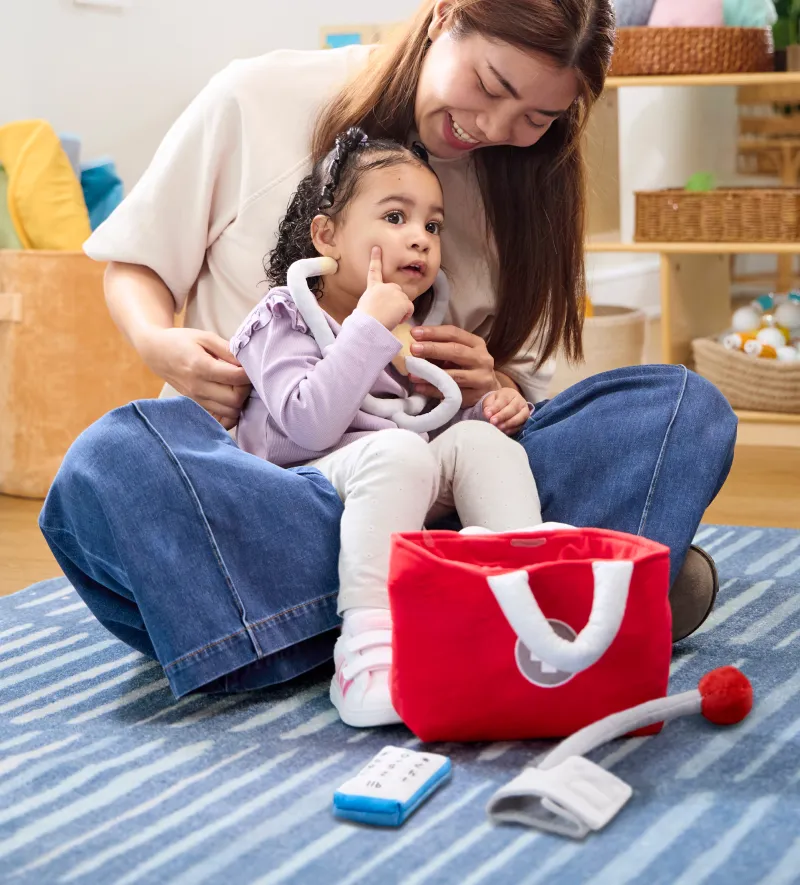 Child on a colorful carpet in a classroom reaching into a basket of soft toys