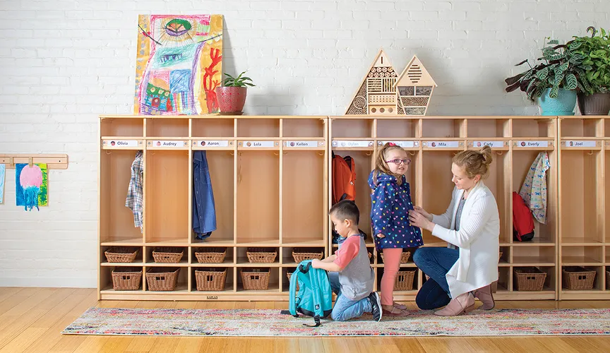 Teacher helping a child unzip a coat in front of Premium Maple locker units
