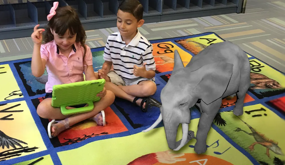Children sitting on an animal themed carpet playing a game on a tablet with a 3D elephant shown next to them