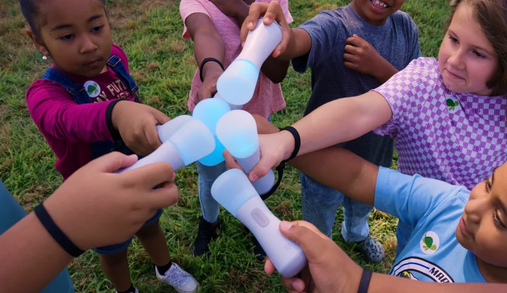 Children outside in a circle touching small handheld devices with colorful lights on the ends