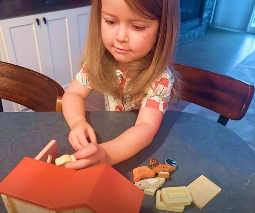 Child playing with a wooden toy barn and farm animals