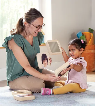 Teacher showing a toddler soft blocks with faces on them