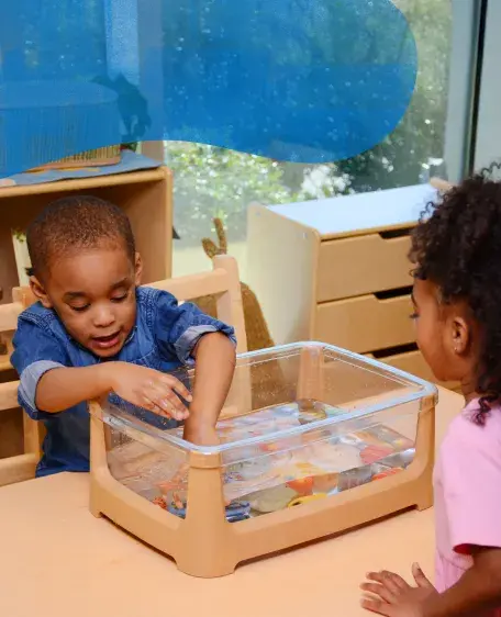 Two preschool children reaching into a small tank of water to grab small toys
