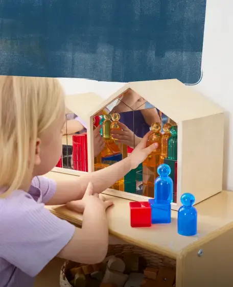 Girl playing with colorful transluscent figures in a house-shaped wooden box with mirrors on the inside
